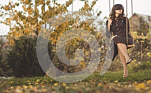 Cute girl in a dress sways on swing in the autumn garden, a young woman in a positive romance mood relaxing on nature