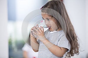 Cute girl drinking glass of water at home photo