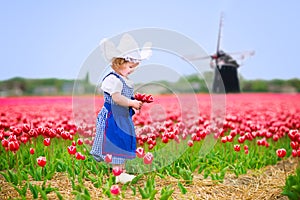 Cute girl in Dutch costume in tulips field with windmill