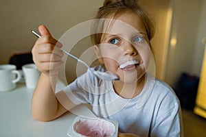 Cute girl eats yogur with appetite, has dirty mouth, has fun, grimaces photo