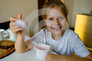 Cute girl eats yogur with appetite, has dirty mouth, has fun, grimaces photo