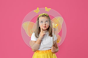 Cute girl in fairy costume with yellow wings and magic wand on pink background