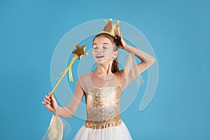 Cute girl in fairy dress with golden crown and magic wand on light blue background. Little princess
