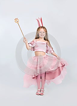 Cute girl in fairy dress with pink crown and magic wand on light grey background. Little princess