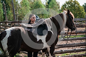Cute girl gets ready for a ride on a horse and saddles it on an autumn day