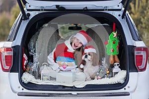 Cute girl is getting ready for Christmas, girl with shih tzu dog in a Santa hat sitting in the car decoration Christmas New Year`