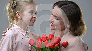 Cute girl giving flowers to beloved mother, surprise for birthday or March 8