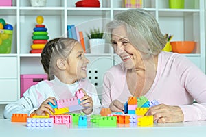 Cute girl and grandmother playing with colorful plastic blocks
