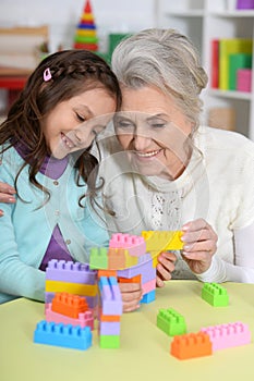 Cute girl and grandmother playing with colorful plastic blocks