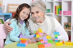 Cute girl and grandmother playing with colorful plastic blocks