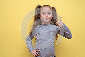 A cute girl in a gray T-shirt shows emotions on a yellow background