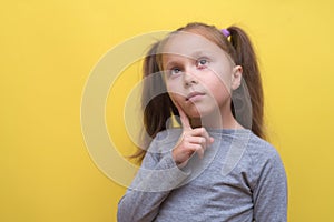 A cute girl in a gray T-shirt shows emotions on a yellow background