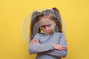 A cute girl in a gray T-shirt shows emotions on a yellow background