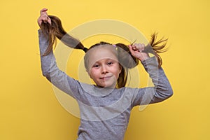 A cute girl in a gray T-shirt shows emotions on a yellow background