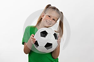 A cute girl in a green t-shirt with a soccer ball in her hand smiles isolated on a white background. A sporty caucasian kid holds