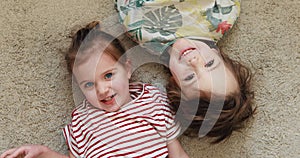 Cute girl with happy brother lies on floor with beige carpet