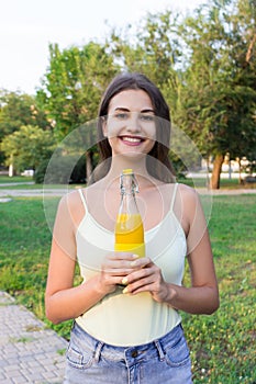 Cute girl is having a walk in the park holding a bottle of orange juice in a sunny wam day