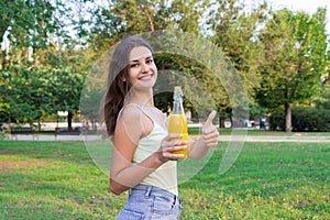 Cute girl is having a walk in the park holding a bottle of orange juice in a sunny wam day