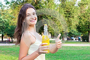 Cute girl is having a walk in the park holding a bottle of orange juice in a sunny wam day