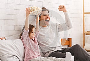 Cute girl and her father watching football match on TV