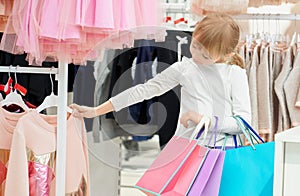 Cute girl holding bags and choosing pink sweater in store