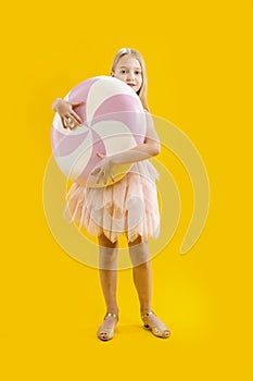 A cute girl is holding a huge pink and white candy on a yellow background. Sweet gift. Large lollipop. Christmas sweetness.