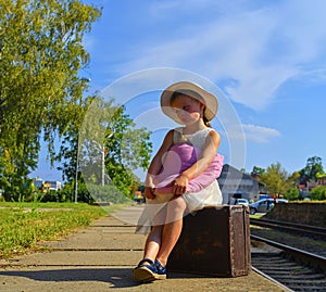 Cute girl holding plush toy on a railway station, waiting for the train with vintage suitcase. Traveling, holiday and chilhood con