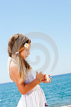 Cute girl holding shells on sunny beach.