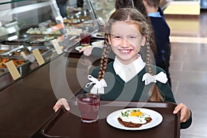 Cute girl holding tray with healthy food in canteen