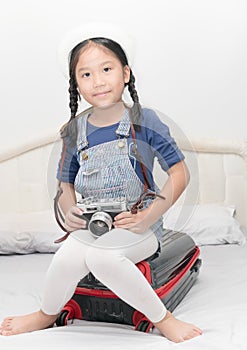 Cute girl holding vintage camera and sit on suitcase