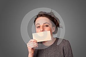 Cute girl holding white card at front of her lips with copy space