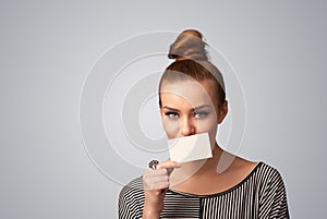 Cute girl holding white card at front of her lips with copy space