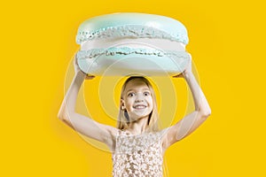 A cute girl holds a huge blue macaroons above her head on a yellow background. Sweet gift. Round dessert. Christmas sweetness