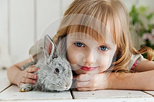Cute girl hugging with rabbit while lying on the floor at home