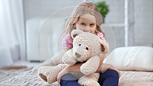 Cute girl hugging toy bear sitting on bed at cosiness bedroom. Shot on RED Raven 4k Cinema Camera