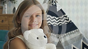 Cute girl is hugging a white teddy bear, looking at camera and smiling