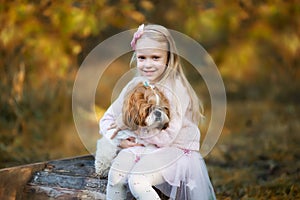 A cute girl hugs a Shih Tzu dog in the autumn forest. A girl walks with a dog in an autumn park