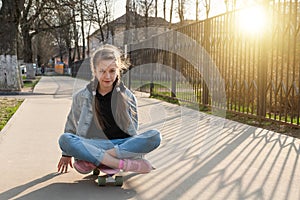 Cute girl in jeans and pink sneakers rides a penny skate longboard around the city. International Skateboarding Day.