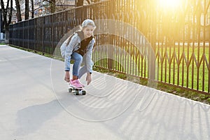 cute girl in jeans and pink sneakers rides a penny skate longboard around the city. International Skateboarding Day.