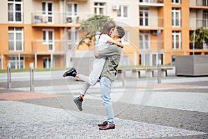 Cute girl jumping to man sunny, summer day. Stylish couple in love hugging and kissing in city street. Relationship, active lifest