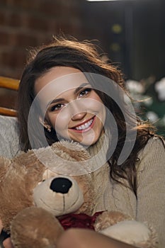 Cute girl in knee socks and sweater with Teddy bear in her hands sitting in armchair in fancy room