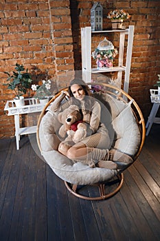 Cute girl in knee socks and sweater with Teddy bear in her hands sitting in armchair in fancy room