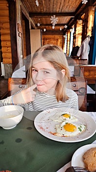 cute girl licks her finger at breakfast with scrambled eggs.