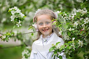 Cute girl listening to music in an apple blossom tree. adorable blonde enjoying music in headphones outdoors in a park. Children`