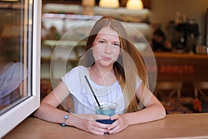 Cute girl looking out of the window and drinking blue lemonade