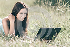 Cute girl looking at the screen of her laptop while lying on the grass