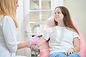 Cute girl looks at oncologist doctor with dermatoscope in hand