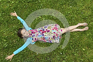 Cute girl lying on the grass, arms outstretched, top view.