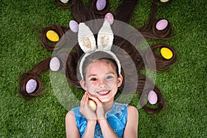 Cute girl lying on the grass with Easter eggs. Easter eggs are in her hair