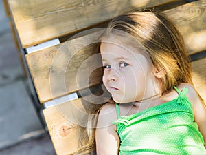 Cute girl lying on wooden bench looking at camera with scepticism